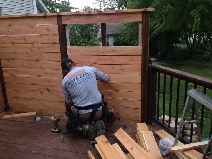Worker building horizontal wood privacy screen on a residential deck project in North Liberty, Iowa.