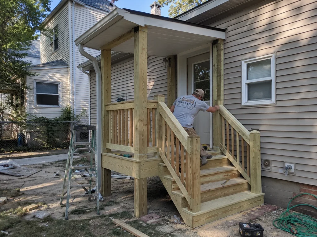Worker building small covered porch and stairs on a residential deck project in Coralville, Iowa.