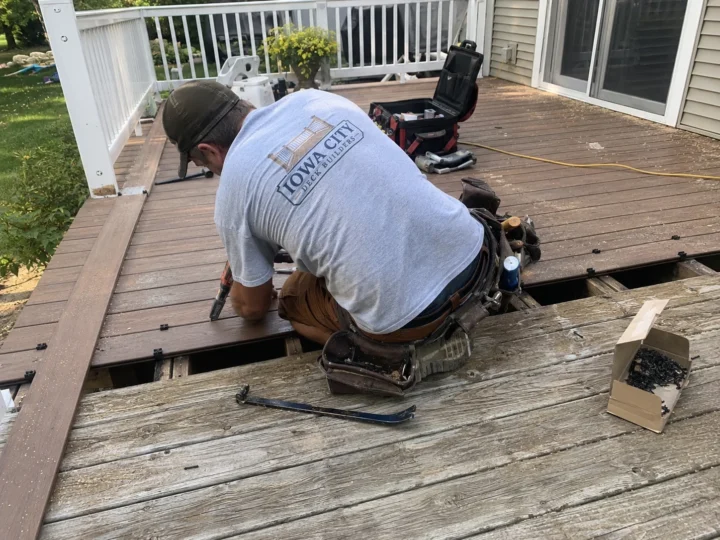 Worker cutting and replacing deck boards on a residential deck project in Hills, Iowa.