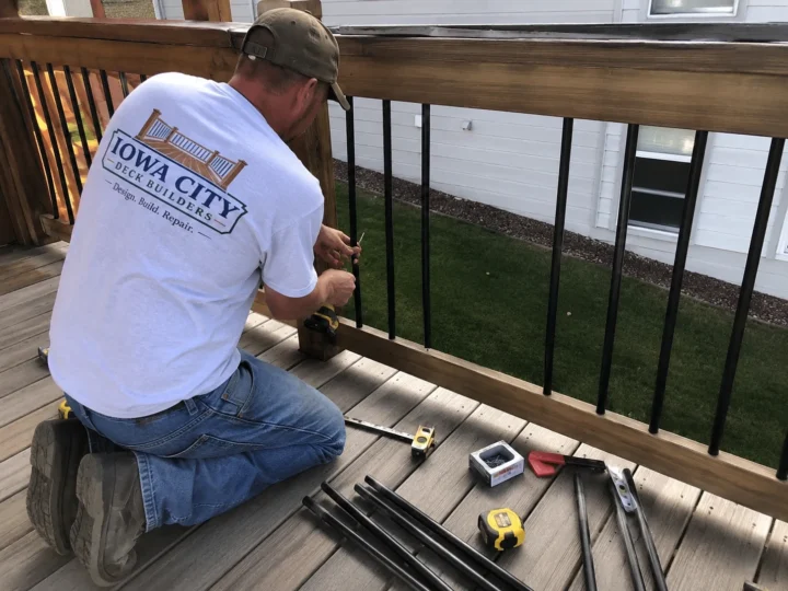 Worker installing black metal deck balusters on a residential deck project in Marengo, Iowa.