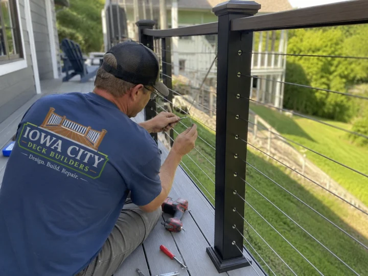 Worker installing cable deck railing post on a residential deck project in Iowa City, Iowa.