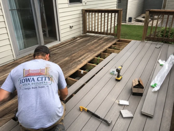 Worker installing composite decking over frame on a residential deck project in Oxford, Iowa.