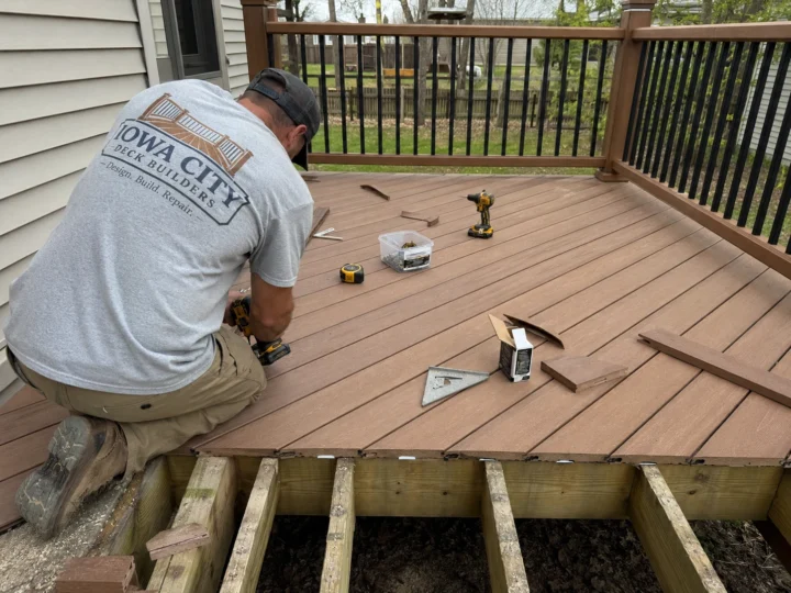 Worker installing composite decking on a residential deck project in Riverside, Iowa.