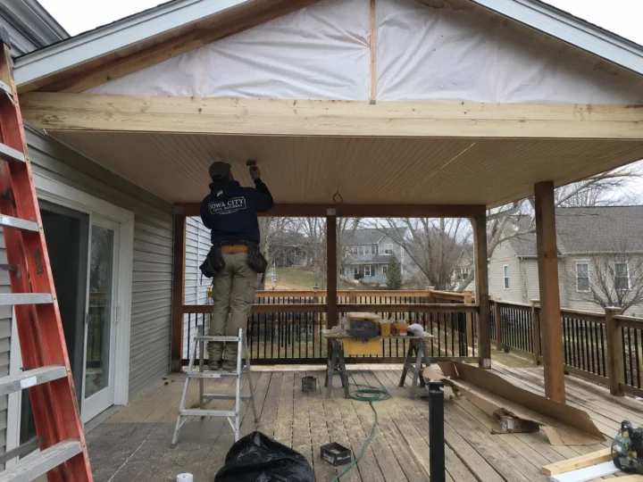 Worker installing covered deck roof and ceiling on a residential deck project in West Branch, Iowa.