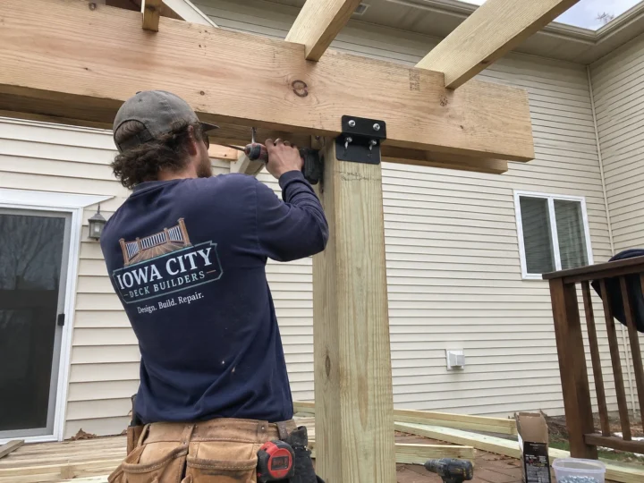 Worker installing deck post and beam hardware during deck support work in West Branch, Iowa.
