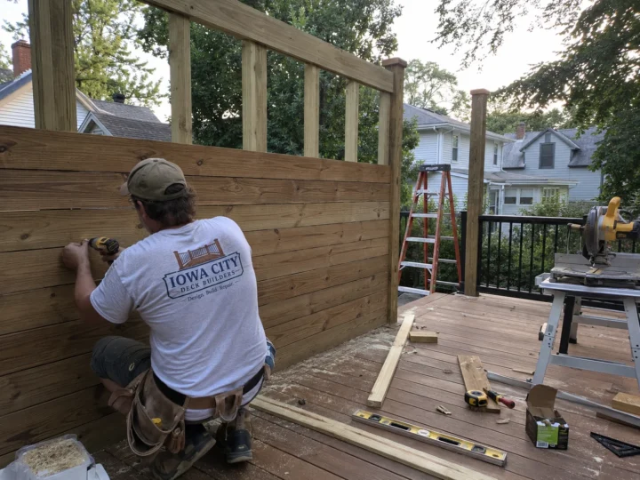 Worker installing horizontal wood privacy screen on a residential deck project in Nichols, Iowa.
