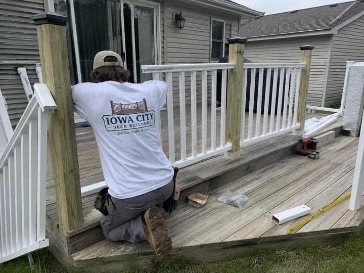 Worker installing white deck railing on a residential deck project in Iowa City, Iowa.