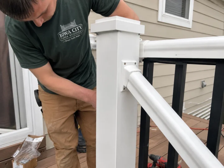 Worker installing white vinyl railing hardware on a residential deck project in Iowa City, Iowa.