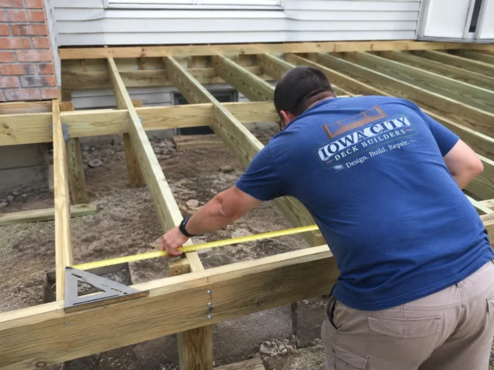 Worker measuring ground level deck frame on a residential deck project in Oxford, Iowa.