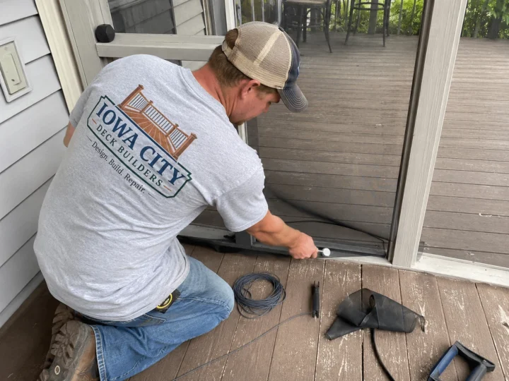 Worker preparing deck board near patio door on a residential deck project in Amana, Iowa.