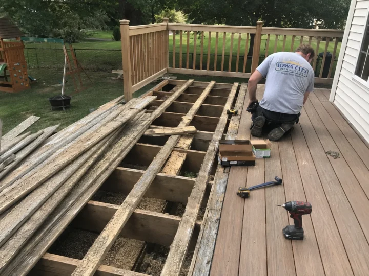 Worker rebuilding deck boards over exposed joists on a residential deck project in Marengo, Iowa.