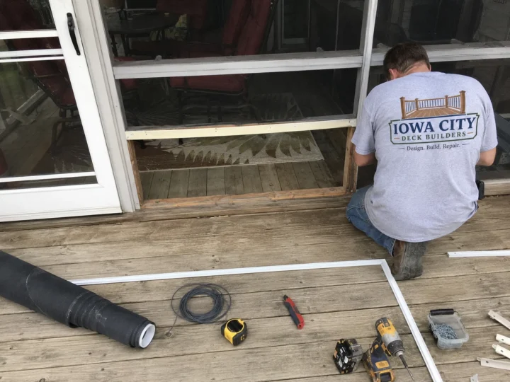 Worker repairing deck entry at patio door on a residential deck project in Marengo, Iowa.
