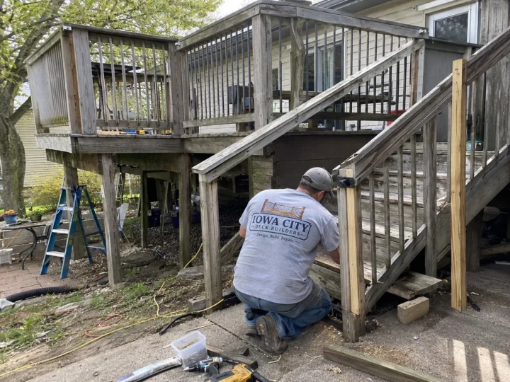 Worker repairing weathered deck stairs on a residential deck project in Riverside, Iowa.