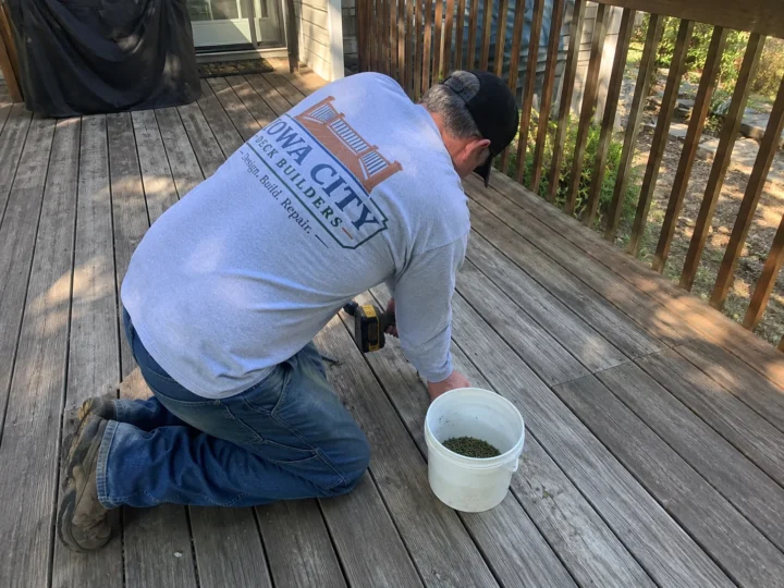 Worker repairing weathered deck surface on a residential deck project in Shueyville, Iowa.
