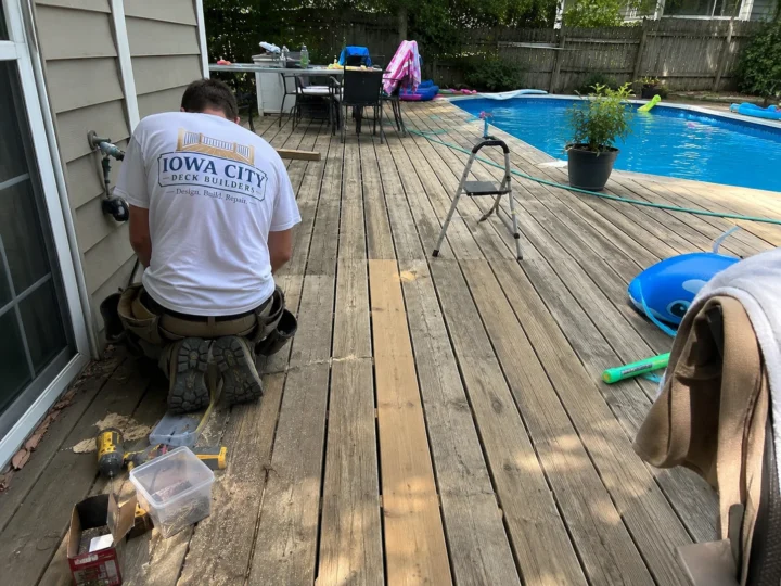 Worker replacing damaged poolside deck boards during deck repair in Iowa City, Iowa.
