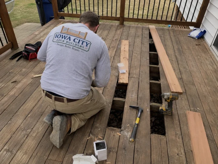 Worker replacing weathered deck boards on a residential deck project in Marengo, Iowa.