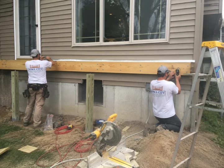 Workers installing deck ledger and framing during structural deck work in Tiffin, Iowa.